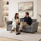 A man and a woman sit on a gray upholstered loveseat sofa