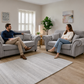 A man and a woman sit on matching light gray tufted armchairs 